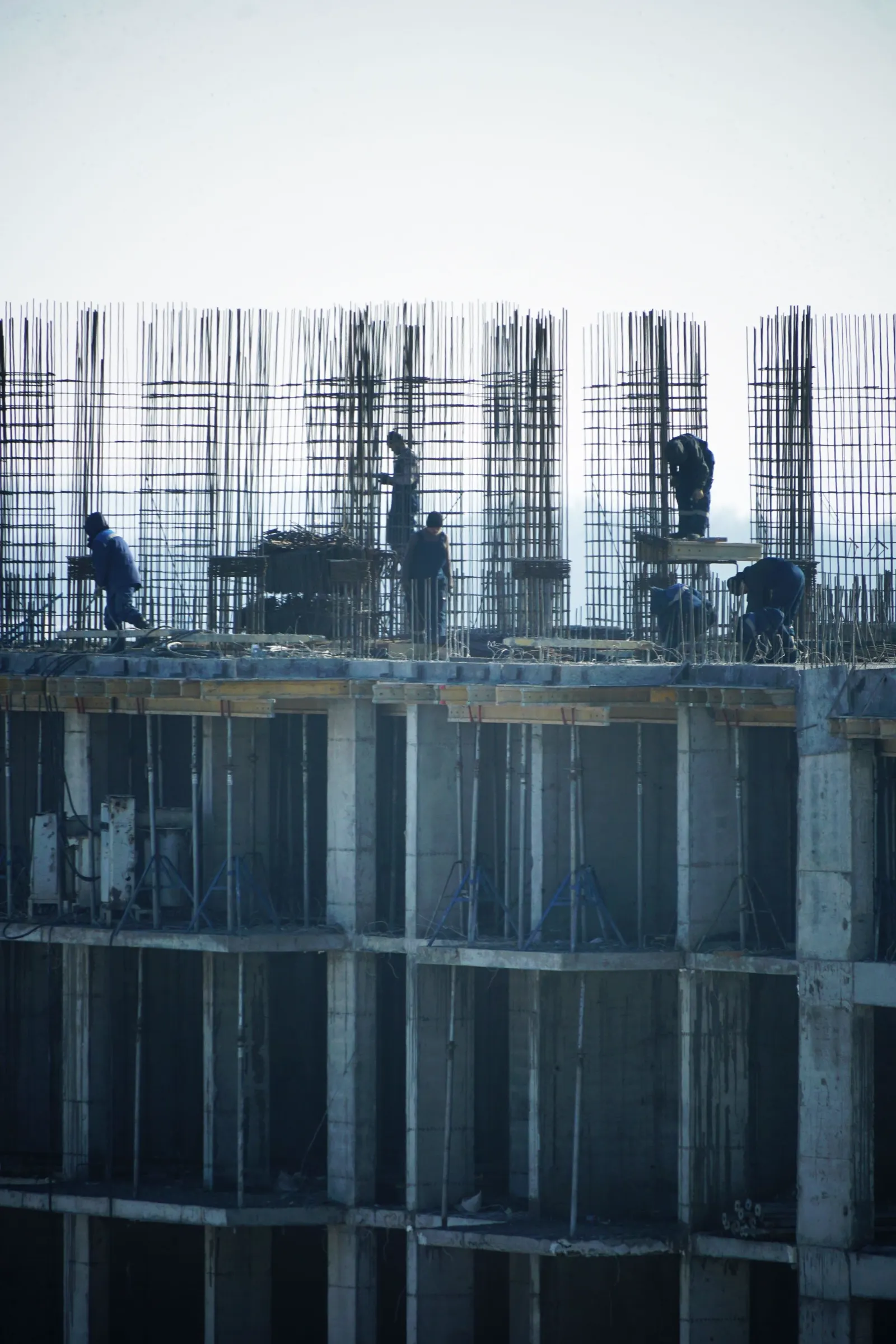 Munkások pillérvasalást kötnek egy monolit vasbeton épület legfelső szintjén, a kiálló betonacélok között